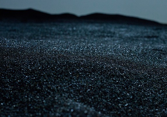 Closeup of the sparkling black sand that covers the floor of the gallery. It looks like it's being illuminated by moonlight.