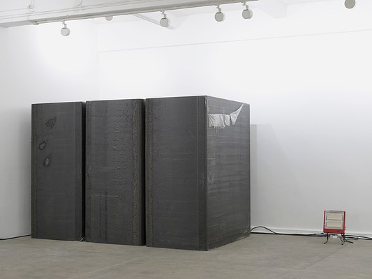 A right-angle view of the row of three foam blocks spaced close together, and a portable red space heater to their right. From this angle we can see that they are deeper than they are wide, and there appears to be a bit of plastic sheeting peeling off the side of the right-most block from the top. They seem to have a rubbery or gummy texture like a yoga mat.