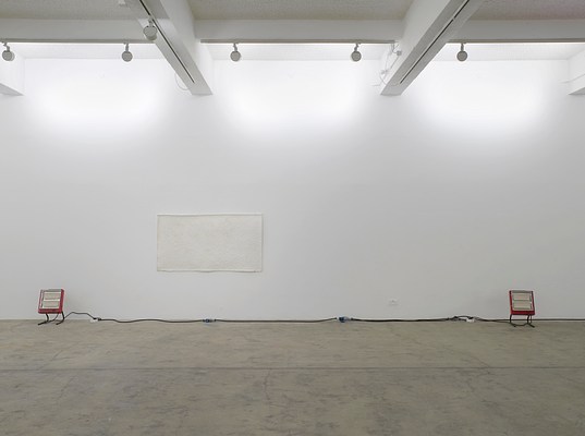 Installation view showing two portable red space heaters flanking an off-white rectangular piece on the wall directly in front of us.