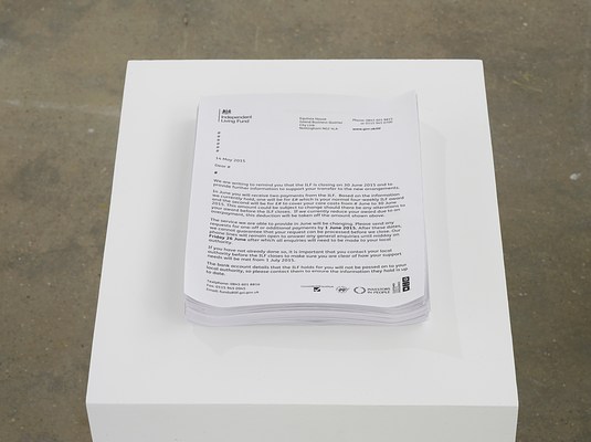 Close-up view of a stack of standard letter-sized papers with printed text on a white pedestal. On the top of the stack is a letter printed on Independent Living Fund letterhead dated 14 May 2015 that details the termination of payments received from ILF. Exact amounts have been replaced with a pound sign.