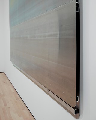Close-up, right-angle view of the large, silver-metallic wall work showing the bottom right corner where the front and back panels are affixed to the structural metal beams. There is a gap of what looks like an inch or two between the front and back panels. From this angle, the surface texture of the industrial metal sheeting is more pronounced.