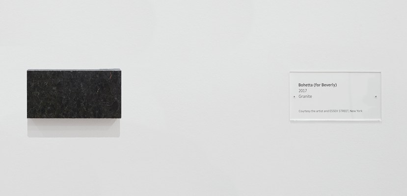 Close-up view of the blank, granite block with a wall label containing work details on our right. The label, or what's traditionally called a "tombstone," seems to have the exact same dimensions as the granite block.