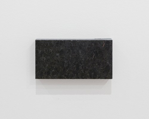 Close-up view of the blank granite block where it's possible to see its veins and mottled, dark grey surface.