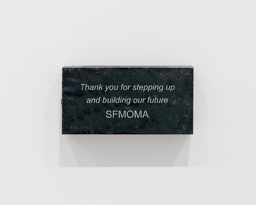 Close up view of a dark grey, rectangular granite block with the following words etched or printed onto its surface: "Thank you for stepping up and building our future SFMOMA"