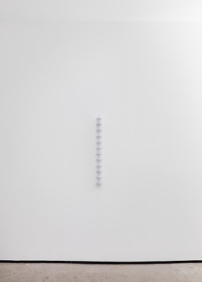 A slightly curved white wall with a hanging sculpture.