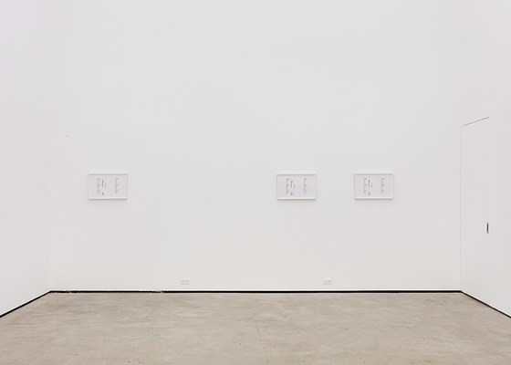 A large white wall with three framed artworks unevenly spaced.