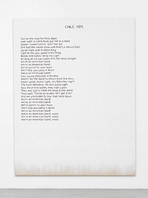 Close view of one of the paintings in the previous installation views. The painting is white except for around the bottom edge, where we can see the raw cotton canvas faded in. Against the white background, we can see a block of black text aligned to the left margin, and a title in capital letters at the top in the center. The text appears hand written, neatly, in sans serif. The title reads "Chile, 1973" written in all caps and the block of text reads:. "Out on the road for forty days. Last night in Little Rock put me in a haze. Sweet sweet Connie doin' her act. She had the whole show and that's a natural fact. Up all night with Freddie King. I got to tell you, poker's his thing. Booze and ladies keep me right. As long as we can make it to the show tonight. We're an American band. We're an American band. We're comin' to your town. We'll help you party it down. We're an American band. For young chiquitas in Omaha. Waitin' for the band to return from the show. Feelin' good, feelin' right, it's a Saturday night. The hotel detective, he was outta sight. Now these fine ladies, they had a plan. They was out to meet the boys in the band. They said, "Come on dudes, let's get it on". And we proceeded to tear that hotel down. We're an American band. We're an American band. We're comin' to your town. We'll help you party it down. We're an American band. We're an American band, wooo. We're an American band, wooo. We're an American band, wooo". . . . 
