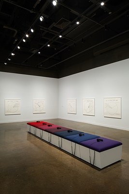 Purple, blue and red cushions on a white bench with 7 headphones are surrounded by 5 pie-chart drawings on 2 walls.