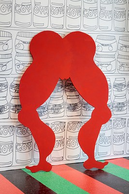 A detail of the bright red cutout of legs and butt seen in previous installation images. The cutout is a silhouette of the free standing sculpture of the woman in the pink bathing suit. Simplified from the details of bathing suit lines, we can see that the rounded butt forms the shape of a heart, ending in the lips of the vulva. All of the shapes on the silhouette of this body are rounded, the thighs, knee caps, calf muscles and feet arches.
