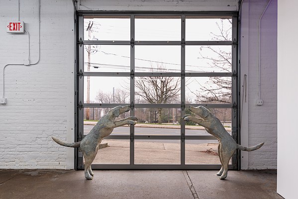 "Dancing with London” is a sculptural installation of 2 dogs, each a representation of the artist’s guide dog, London, who is a golden Labrador Retriever. The dogs are standing up, 53 inches tall on their hind legs and 3 feet apart. They face each other with their front legs extended out in front of their bodies, as if they are about to leap into the air. There is enough space for you to stand between them and hold up each of its paws, like in a dance. Their eyes are closed, with a serene look on their face, with a hint of a smile. The paws are sculpted with details of each little finger, and their nails are glossy and smooth. When you hold onto them, you can feel the underside of the paw is a leathery texture, like the soft padding of a dog’s paw. On the dog’s belly are little nipples, the back has the look of combed fur, and its tail curves up in a swoop.