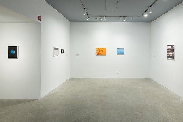 Five framed color photographs and one framed black and white photograph hang on four white walls of the gallery.