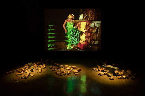Three piles of gold rocks are placed in front of a screen on which a woman in a green dress stands in front of a hearth.
