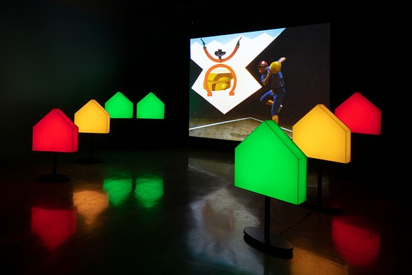 Colored pentagons flank a screen on which an image of a man in a blue jumpsuit and a stick drawing of a cowboy are projected.