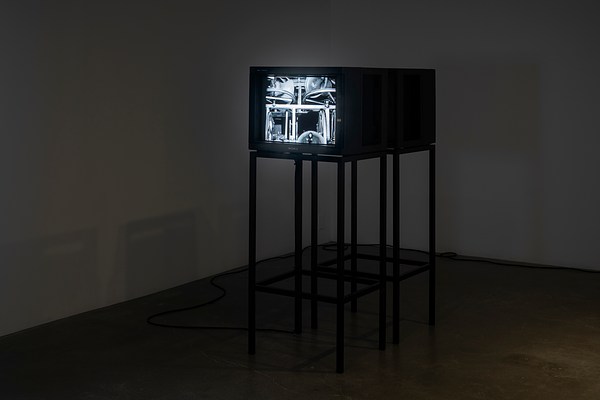 Two video monitors on  stands face in opposite directions in  a darkened room. A black and white  image is visible on one monitor.