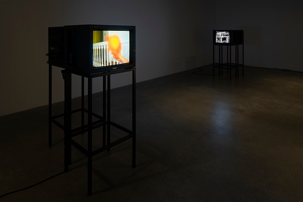 Two sets of video  monitors on stands in a darkened  room, one monitor of each set  facing the viewer, with images  visible on each.