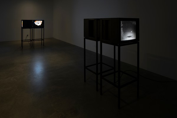 Darkened room with two  paired sets of video monitors on  stands, with black and white images  visible on one of each set.