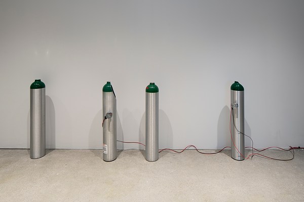 Four silver tanks  with the top painted green.  Two of the tanks have a  portion of the top removed  and wires affixed to the side.
