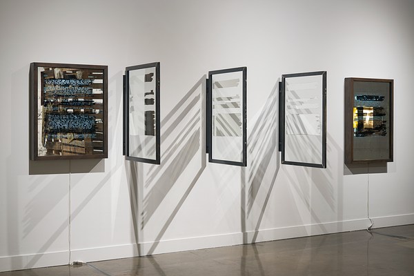 Five wall pieces in a row. Three in the middle with framed glass at 45 degree angles, and a light box with text at each end.&nbsp;