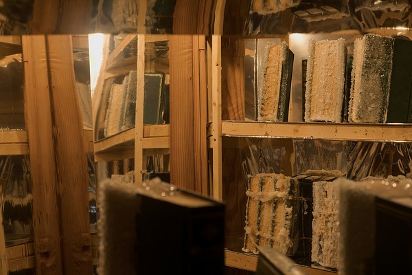A close up view of a tight space filled with wood shelves, a mirror, and sugar encrusted books a similar color as the shelves.&nbsp;