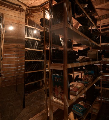 A view from inside an attic like space with dark wood planks, a slanted ceiling, wooden ladders and warm lights.&nbsp;