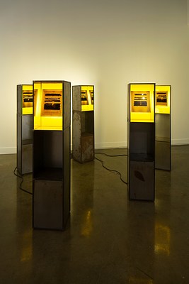 Five light boxes on top of tall podiums with a sheet of paper in each that has certain parts of the text blacked out.&nbsp;