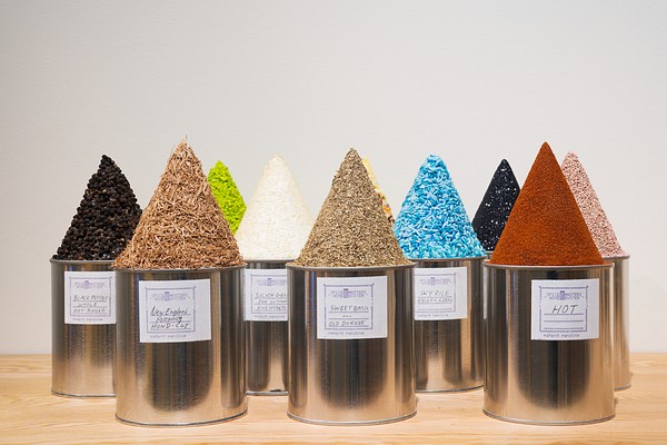 Rows of round tin cans with homemade white labels holding cone shaped mounds of various colored substances and texture.
