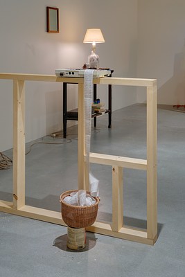 A small computer/ printer on a ledge, paper spooled over into a woven basket on top of a paint can, a lighted lamp in back.