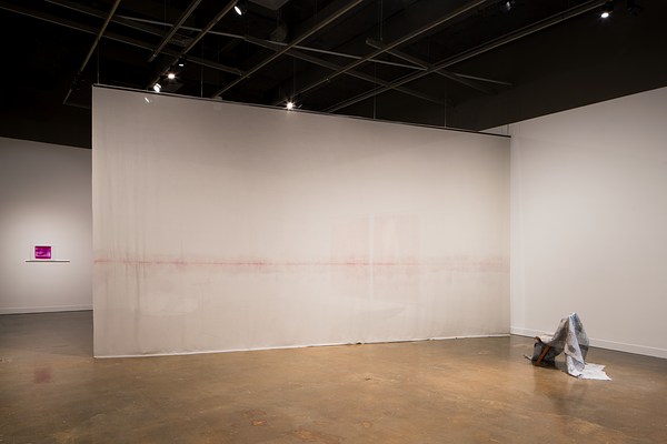 Installation view of a space with a large hanging cloth, two small prints, a yellow and a purple, a cloth folded over a chair.