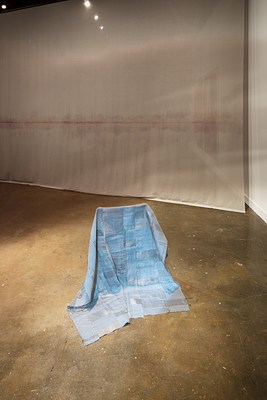  A blue-ish white fabric with conductive and reflective thread draped over a folding chair, a hanging fabric piece in back.