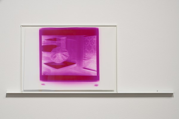 A saturated purple and white print behind glass on a white wall, a thin shelf running underneath.