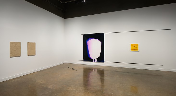 A corner space, two clay tablets on left wall, a large abstract print and a small yellow and black print on wall to the right.