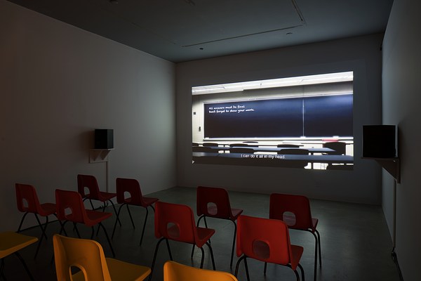 A darkened space with chairs and a projection of a blackboard with text, and the caption “I can do it all in my head”