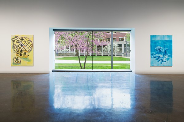Flowering trees show through a picture window, flanked by a yellow painting on the left and a blue painting on the right