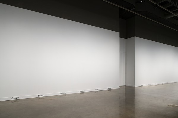 Words including Freezy, Sneezy, Wheezy line the baseboard of a blank gallery wall, with an alcove break in the center.