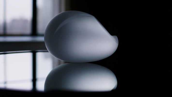 Video still closeup of frosted oval object on mirror, which reflects both the object and blurry window light on the left side.