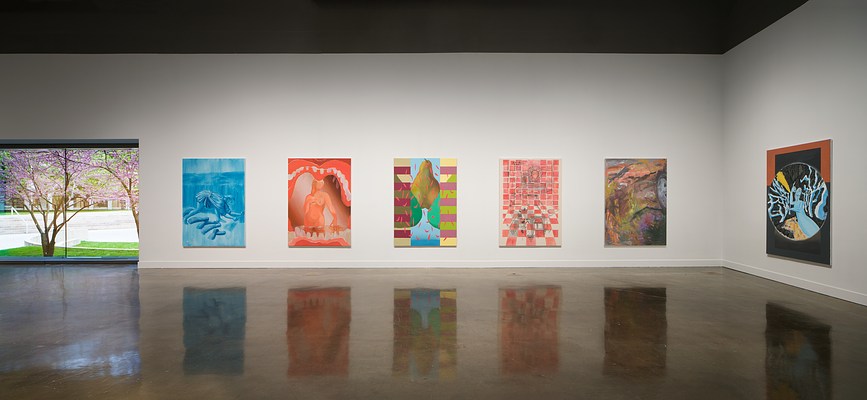 Five colorful paintings hang next to a large window showing a flowering tree, one painting hangs on the intersecting wall.