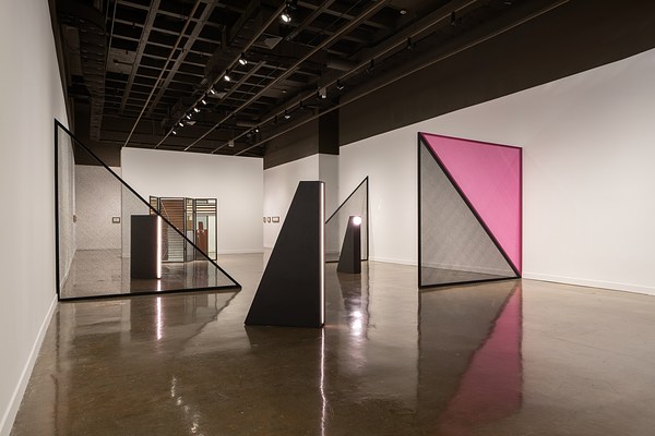 A juxtaposition of black triangular light sculptures, with large mesh black and pink  triangles and a mirrored folding screen.
