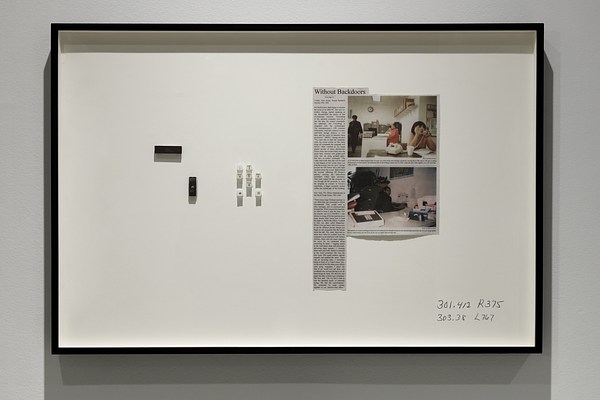 Framed artwork with 2 computer chips, 6 phone buttons, a newspaper clipping, and 2 silkscreened library call numbers  on bottom.