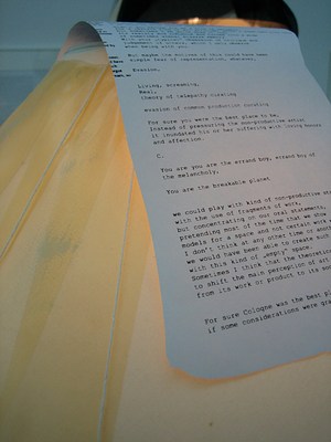 A detail of a lampshade draped with a page of text written by a typewriter. Part of the page is readable after zooming: . . "Living, screaming, . Real, . theory of telepathy curating . . evasion of common production curating . . For sure you were the best place to be, . Instead of pressuring the non-productive artist . It inundated his or her suffering with loving honors . and affection. . . C.. . You are you are the errand boy, errand boy of . the melancholy,. . You are the breakable planet"