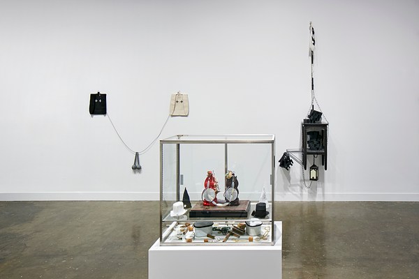 Installation view featuring a glass box with small objects inside and sculptures hanging on the wall behind.&nbsp;