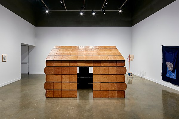 Installation view of Nayland Blake's gingerbread house installation is featured at the MIT List Visual Art Center galleries with a blue tapestry on the wall to the right.&nbsp;