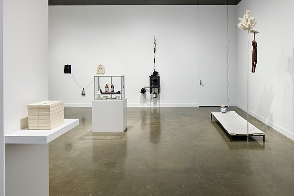Installation view with a rectangular white sculpture on a shelf on the left and various sculptures in the background of different shapes and sizes.&nbsp;