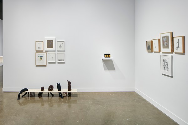 An installation view of Nayland Blake's exhibition at the List Center features soft sculptures held by a plank of wood on a Hershey's chocolate can and small framed prints on the walls to the left and right.&nbsp;
