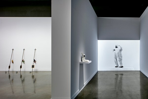 Large projector on the right with a man wearing a bunny costume. On the left, three small sculptures lean against the wall.&nbsp;