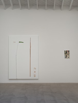Installation view of a gallery space with a white wall and grey, concrete floor. On the white wall, we can see two paintings in portrait format. The painting to the left is large-scale, primed in white, and on its surface we can see a collage of wood sticks, paper, and canvas. The painting to the right is small-scale, and painted in beige, blue, green and back abstract shapes. In the ceiling, we can see narrow white wooden beams protruding perpendicular to the wall. Above them, we can see white planks on the diagonal, making up the ceiling.