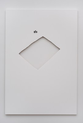 Close view of a painting hanging on a white wall, seen in previous installation images. The painting is in portrait format, and primed in white. Just above the center of the painting, a rectangle oriented diagonally has been cut out. Through the cut-out, we can see the white wall behind the painting, and a drop shadow below the upper edges of the rectangular hole. Slightly above the cut-out, and to the left, we can see the word "ufo" in lower case black letters in sans-serif font. The text appears stenciled onto the canvas, and is slightly smudged. Below the painting, we can see a subtle drop shadow on the wall.