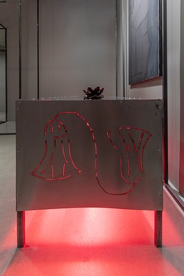 Side view of a stainless steel table lit from underneath with red heating lamps. The light shines through welding on the side of the table and a water lily shaped incense sits on top of the table.