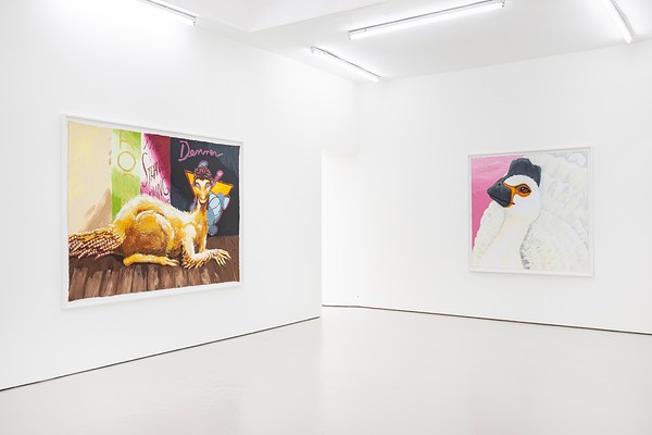 An installation view of the corner of a brightly lit gallery. On our left, a large horizontal painting of a large gold dinosaur sits like a sphinx or cat. On our right, a mostly white painting of a white dinosaur with a black beak and black feathered crown. A black eye is surrounded by orange. The only area not filled in by the dinosaur is a pale pink corner of background.