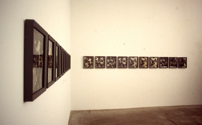 Grainy photograph showing an installation view of two white walls forming a corner of a gallery. On each wall is a row of framed pictures. The row on our left has a steep perspective, while on our right the row of ten framed pictures is nearly flat or parallel to the picture plane. In both cases, the subject matter is difficult to make out, but there appears to be some repetition from picture to picture.