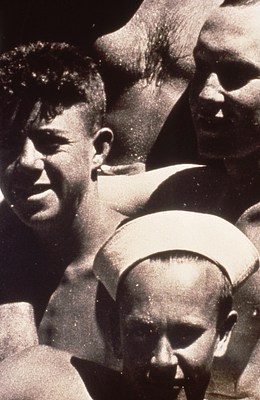 An even closer crop of the image of the reclining figure in what looks like a sailor's cap in the foreground taking up the bottom third of the image. Behind him are two young men with their arms draped over each other's shoulders. And behind them is a bare torso with a hairy chest.